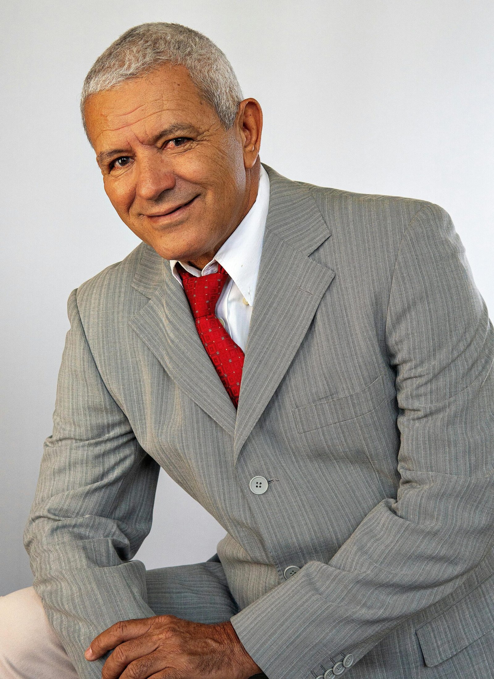 Portrait of an elderly businessman in a grey suit and red tie, exuding confidence and charm.