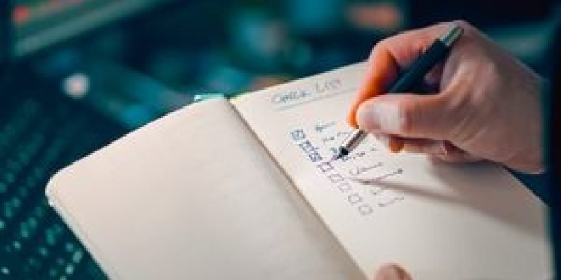 Close-up of a hand writing in a notebook with a checklist for effective task management.